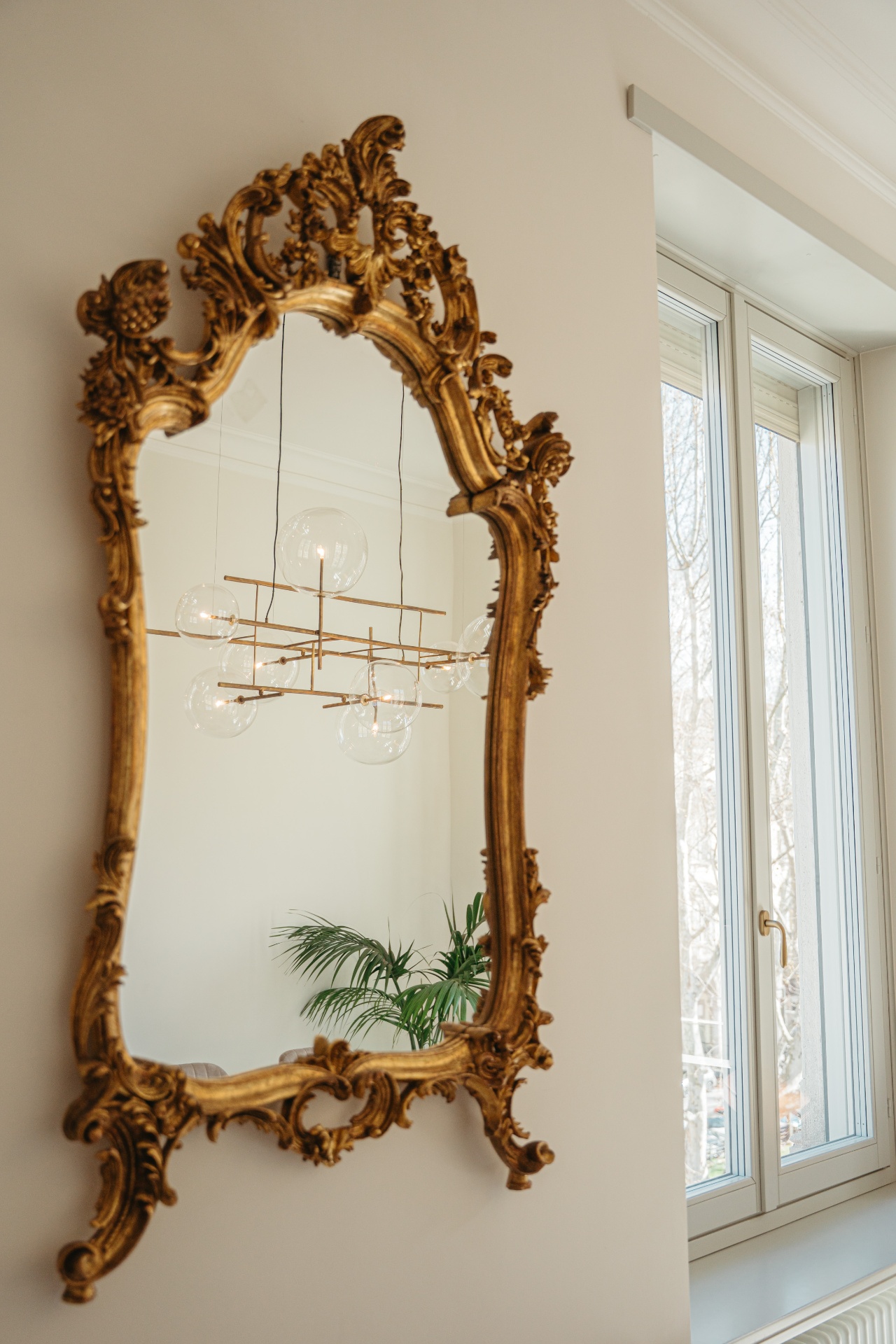 Specchiera dorata in stile rococò riflette il lampadario contemporaneo dello Studio Saglietti Bianco